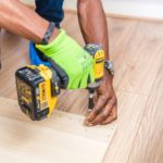 Worker drilling into a wooden floor with a cordless drill