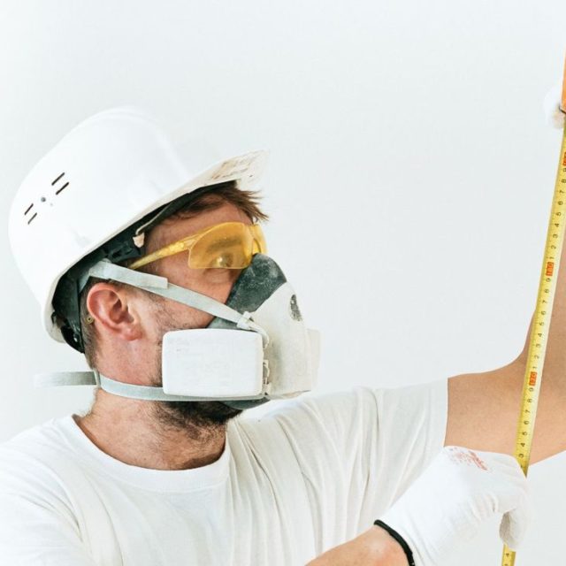 Worker in a respirator and goggles holding a tape measure