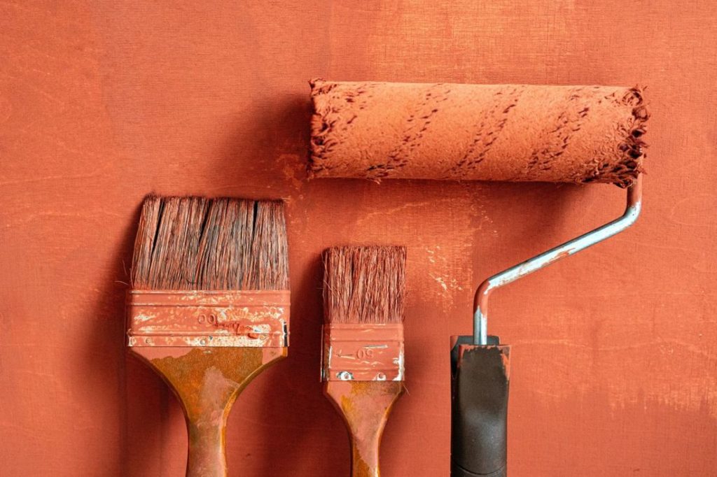 Paint brushes and a roller on an orange wall