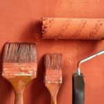 Paint brushes and a roller on an orange wall
