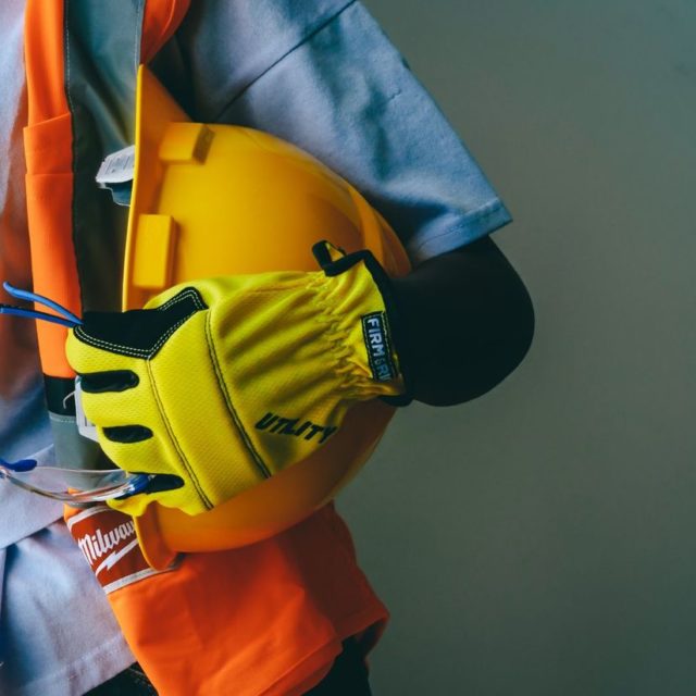 Hands holding a yellow hard hat and safety goggles